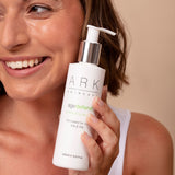 Female model holding ARK's Conditioning Cleanser with bright, healthy-looking skin. Vegan Friendly & cruelty free